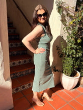 Woman in a green and white striped dress standing on a tiled patio with plants and stairs in the background.