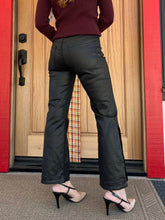 A person shown from the back wearing black wide-leg cropped pants with side slit details, a burgundy sweater, and beige high heels, standing in front of a wooden door with red trim.