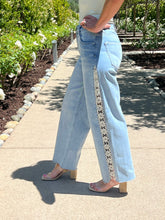 Person wearing light blue jeans with a decorative lace side stripe in a garden setting