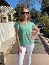 Woman wearing a green striped shirt and white pants standing outdoors.