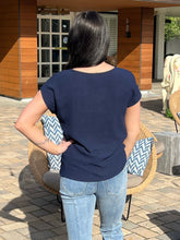Person wearing a navy blue top and light blue jeans sitting on a chair with a patterned cushion.