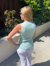 Woman wearing a light blue sleeveless top and white pants standing outdoors.