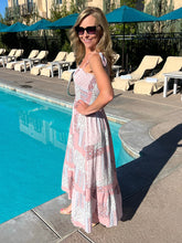 Woman in a pink dress standing by a poolside with lounge chairs and umbrellas in the background.