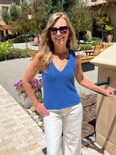 Woman wearing a blue top and white pants standing outdoors.
