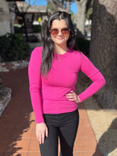 Woman wearing a fuchsia long-sleeve top and black pants standing outdoors.