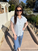 Woman standing outdoors on a sunny day, wearing sunglasses and a blue and white striped shirt.