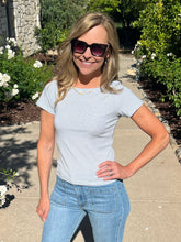 Woman wearing a striped shirt and jeans standing outdoors with greenery in the background