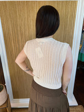 Person wearing a beige knitted vest and brown skirt standing in front of a mirror.