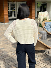 Person wearing a beige sweater and dark pants standing outdoors on a patio.