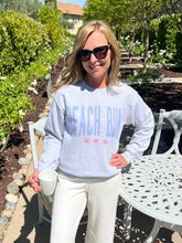 Woman wearing a 'Beach Bum' sweatshirt in a garden setting