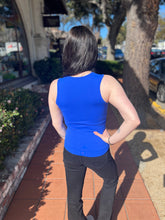 Person wearing a blue sleeveless top and black pants standing on a sidewalk.