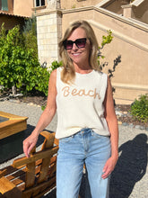 Woman wearing a sleeveless top with 'Beach' text in an outdoor setting