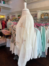 White sweater with star patterns on a mannequin in a store setting.