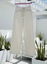 Natural drawstring pants hanging on a rack with plants and chairs in the background