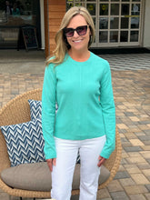 Woman wearing a teal sweater and white pants standing outdoors.