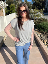 Woman wearing sunglasses and a gray tie  top with blue jeans standing outdoors.