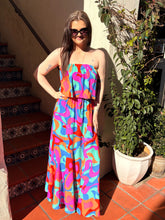 Woman in a colorful strapless dress standing outdoors next to a plant and staircase.