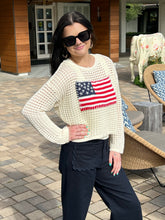 Woman wearing a white sweater with an American flag design outdoors.