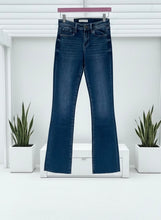 Blue slim bootcut jeans on a hanger with a white background and plants.