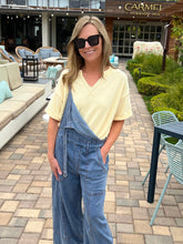 Woman in a yellow top and blue overalls standing on a patio with 'Carmel Mission Inn' in the background.