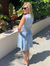 Woman in a light blue dress standing outdoors with greenery in the background
