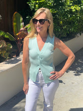 Woman wearing a light green sleeveless top and white pants outdoors.