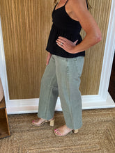 Person wearing light olive barrel jeans and a black top showing side view in a store setting.