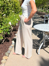 Person wearing a white top and beige wide-leg pants standing outdoors near a garden and table.