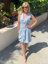 Woman in a light blue dress standing outdoors with greenery in the background