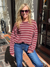 A woman wearing a maroon and white horizontally striped knit sweater and blue jeans, posing outdoors in front of a building entrance.