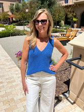Woman wearing a blue top and white pants standing outdoors.