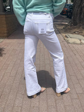 Person wearing light blue sweater and white jeans with a visible brand tag on a sidewalk.
