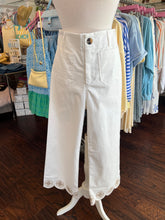 White pants with decorative cuffs displayed on a mannequin against a background of clothing racks.