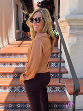 A woman wearing a tan satin long-sleeve top and dark brown pants, standing on outdoor terracotta tiled stairs with a metal railing.