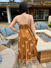 Woman in a brown dress standing in front of outdoor furniture with a building in the background