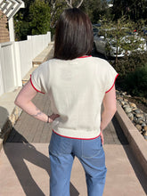 Woman wearing a cream sweater with a red lobster design outdoors.