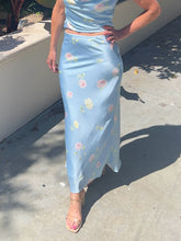 Person wearing a light blue floral dress standing on a sidewalk.