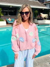 Woman wearing a pink cardigan with shell patterns by a pool