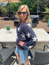 Woman wearing a navy sweater with white star patterns outdoors on a patio.