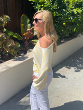 Woman wearing a yellow and white striped sweater and sunglasses, standing outdoors.