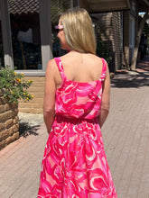Woman wearing a pink floral dress standing on a sidewalk.