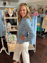 Woman in a chambray shirt and white pants standing in a clothing store.