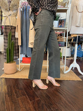 A person standing in a boutique wearing high-waisted, wide-leg gray jeans, a black-and-white patterned top, and beige block-heel sandals. The background shows clothing racks, shelves, and a wooden floor.