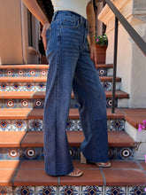 A person wearing high-waisted, wide-leg blue denim jeans stands on terracotta tiled stairs with decorative blue and white mosaic patterns.
