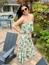 Woman in a strapless dress with green leaf pattern standing outdoors in a garden setting.
