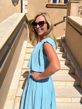 Woman in a light blue top and skirt standing on stone steps outdoors.