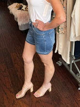 Person wearing a white top and blue denim shorts in a clothing store.