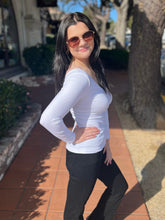 Woman wearing a white long-sleeve top and black pants standing on a sidewalk.