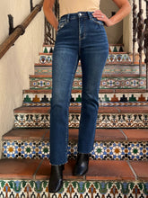 A person wearing dark blue straight-leg denim jeans with frayed hems, paired with black ankle boots, standing on patterned terracotta stairs.