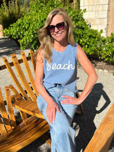 Woman wearing a blue sleeveless top with 'Beach' text, sitting outdoors.